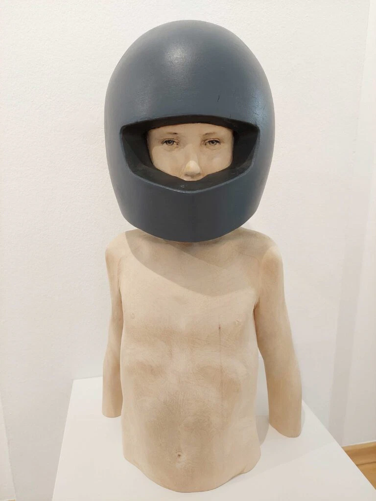 Leo F. Demetz Save in the future Lindenholz, Farbe Höhe 57 cm. Die Skulptur stellt den Torso eines Knaben dar, der einen blauen Motorradhelm trägt.